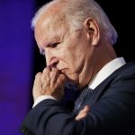 Joe Biden, vestindo um terno, levando a mão à boca com semblante preocupado