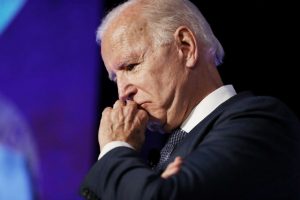 Joe Biden, vestindo um terno, levando a mão à boca com semblante preocupado